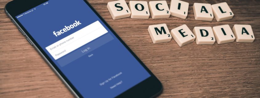 Telefon med Facebooks app på skärmen och orden "social media" i Alfapet-bokstäver